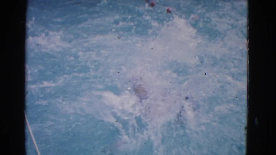 1953 Yonkers 8mm frame with the swimmer mostly obscured by a large splash in blue pool water and faint lane markers.