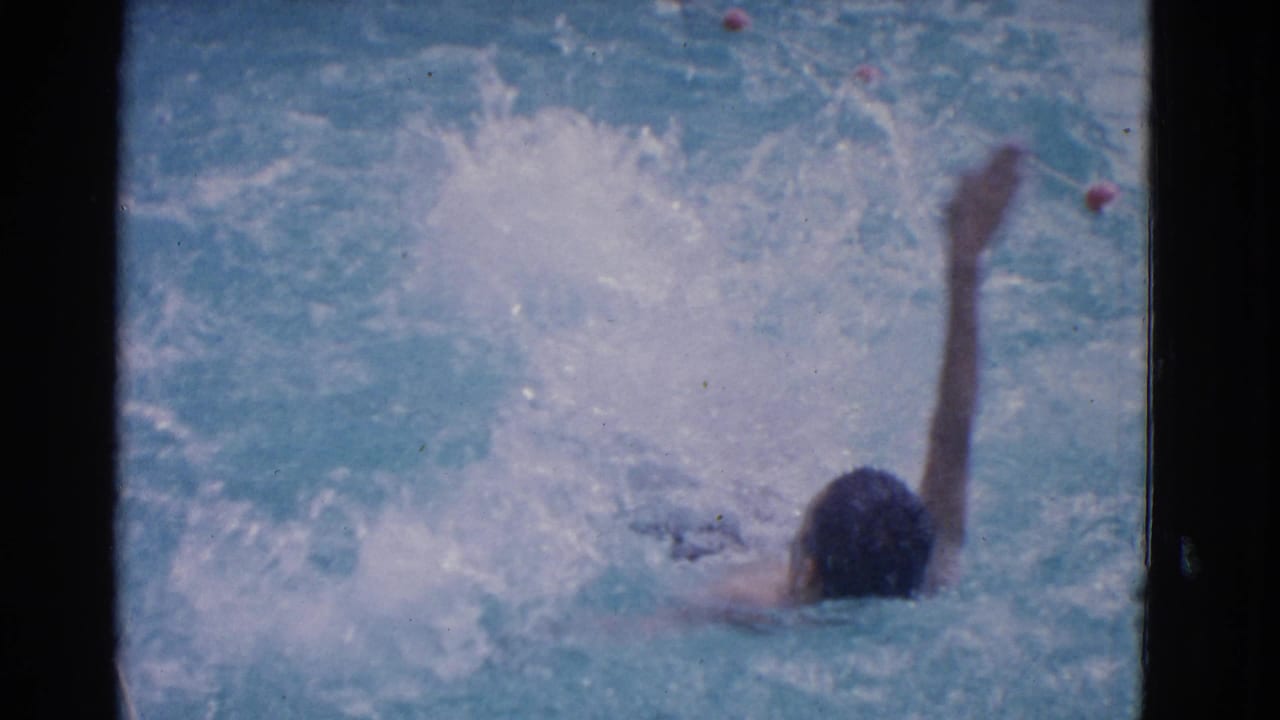 Swimmer in blue pool water raises one arm amid white splashes.