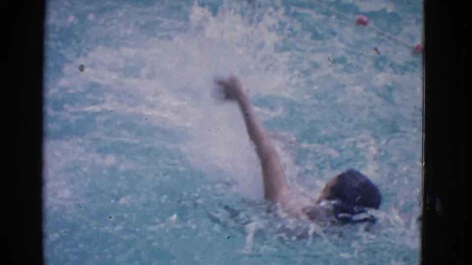 1953 Yonkers pool footage shows a swimmer wearing a dark cap, arm raised during a backstroke-like movement.