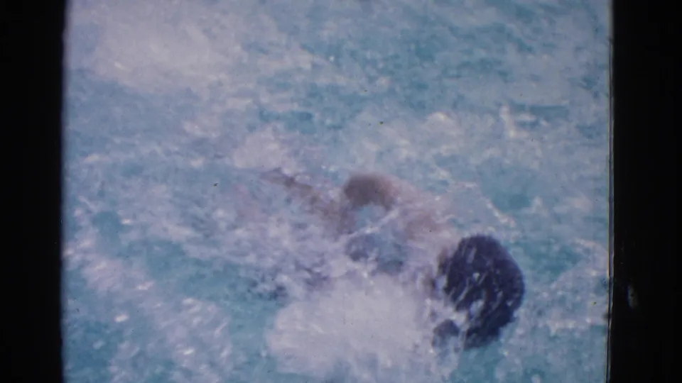 1953 Yonkers home-movie frame with the swimmer low in the pool, partly hidden by bright splashes and soft 8mm grain.