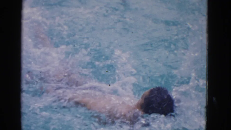 1953 Yonkers pool frame showing the swimmer farther across the water, with a dark cap, visible arm, and trailing splashes.