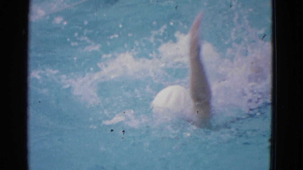 1953 Yonkers home-movie frame showing a woman in a white swim cap swimming freestyle through blue pool water.