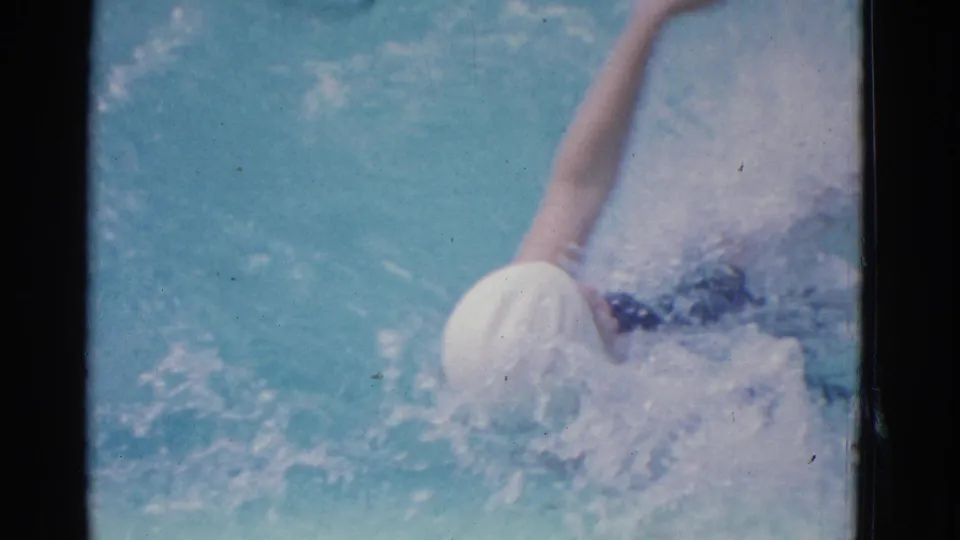 1953 Yonkers pool footage with the swimmer partly submerged, her white cap and arm visible during a freestyle stroke.