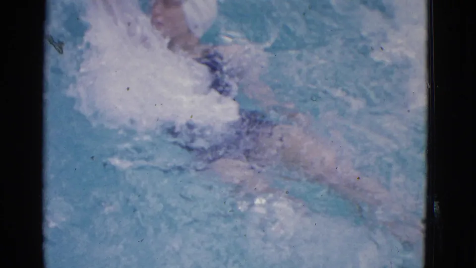 Close 1953 Yonkers home-movie view of a woman swimming in a pool, with her cap, suit, and legs partly visible through splashes.
