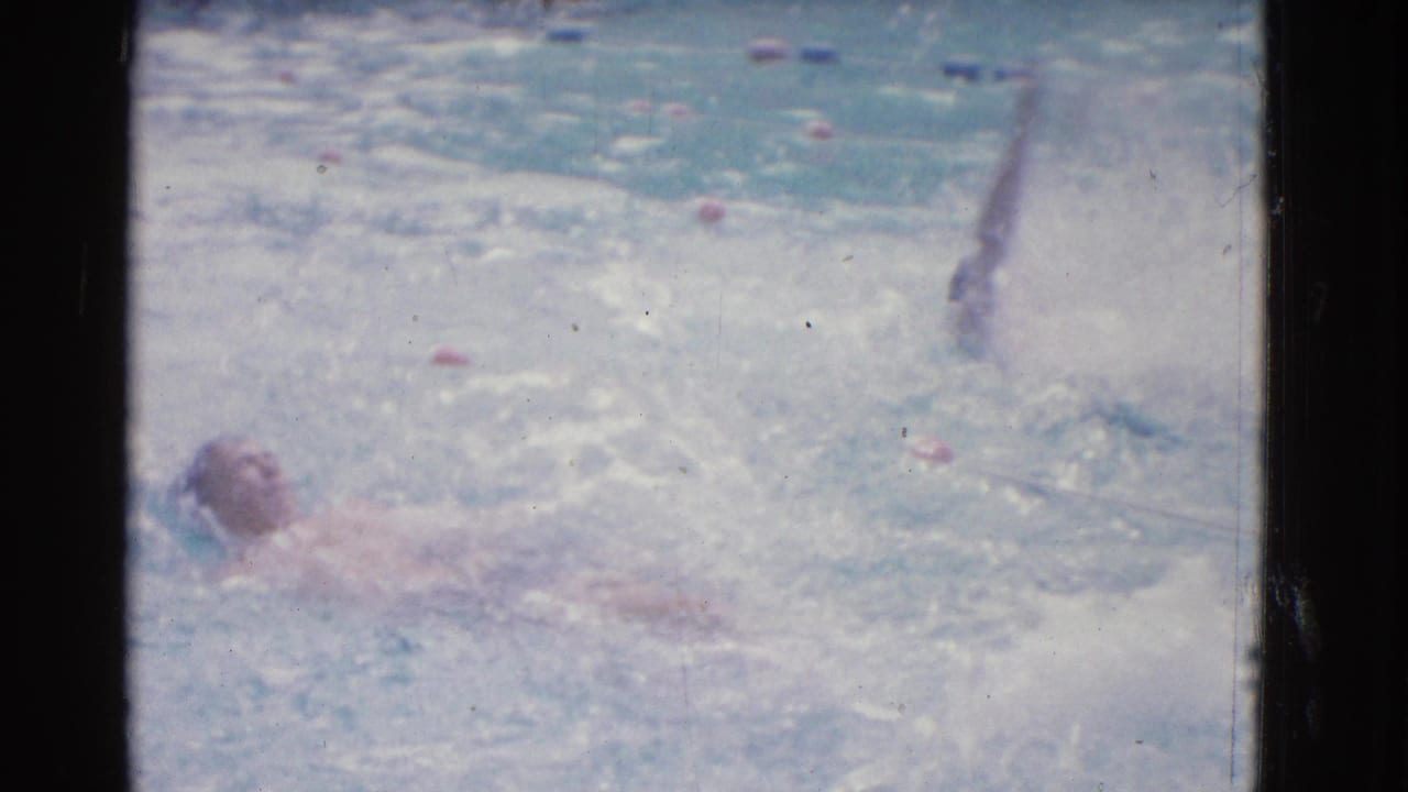 Swimmer on her back moving through an outdoor pool lane with splashing water.
