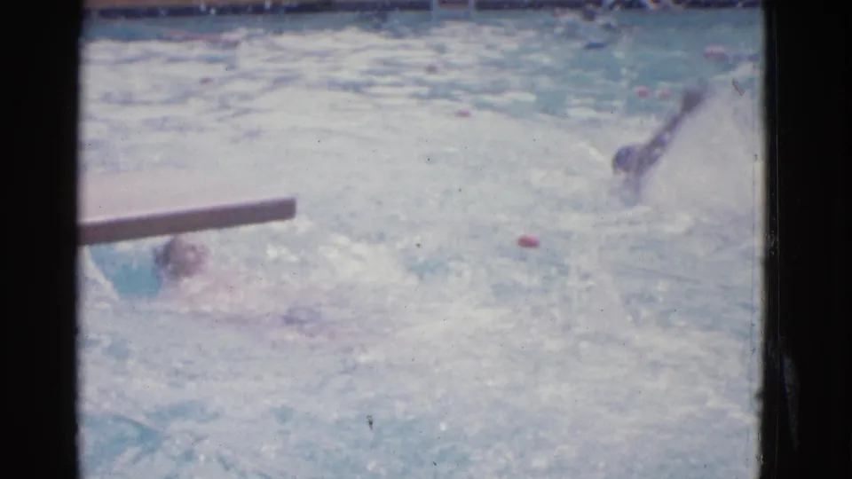 1953 Yonkers poolside view of swimmers doing backstroke, with a foreground rail or bar, lane floats, and washed 8mm color.