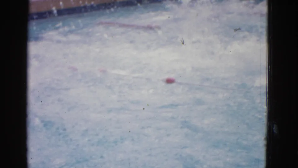 1953 home-movie view of a pool lane in Yonkers, with red buoys and a swimmer largely hidden by bright splashing water.