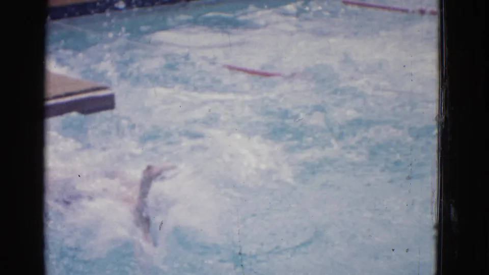 A swimmer surfaces in a Yonkers pool lane, with one arm visible amid splashes near red lane markers and the pool edge.