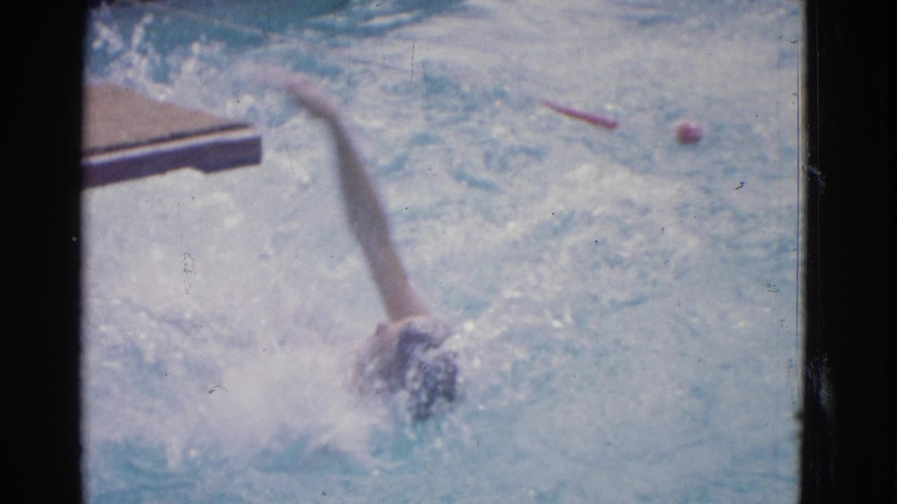 1953 Yonkers 8mm frame showing a swimmer in a dark cap mid-freestyle, partly obscured by splashing pool water.
