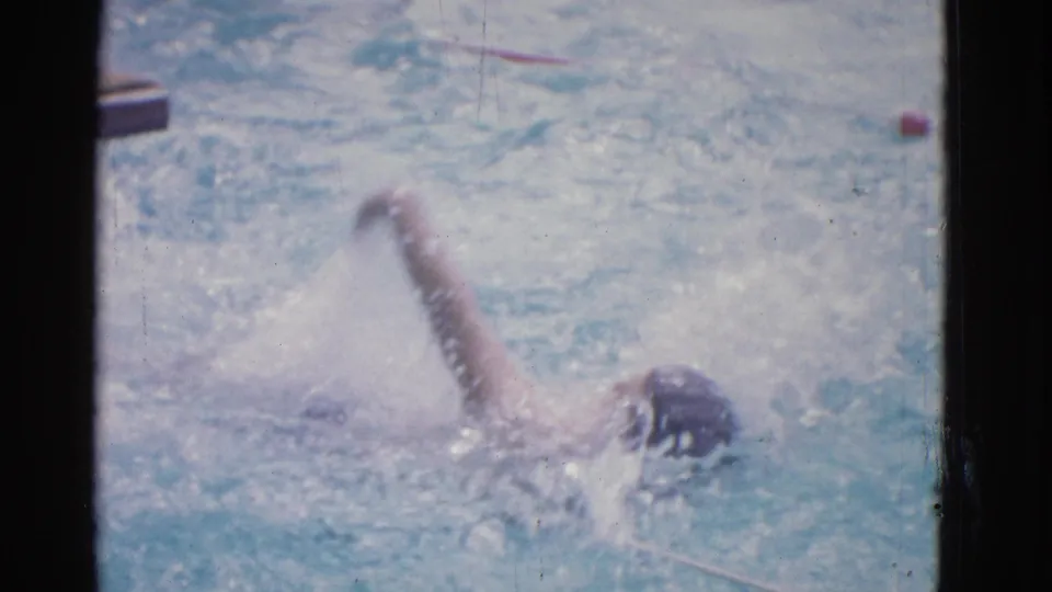 1953 Yonkers pool footage frame with a swimmer’s arm extended during freestyle, surrounded by bright splashes.