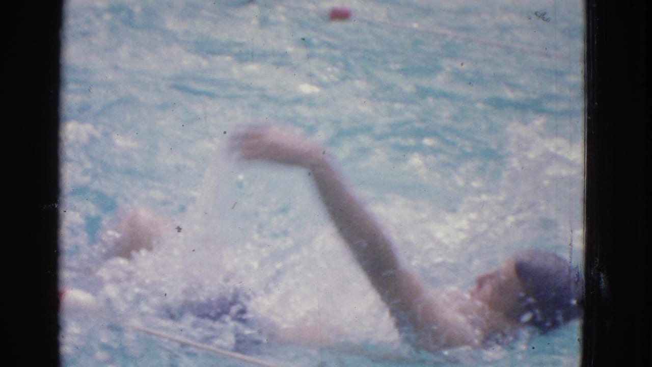 In metadata-supported Yonkers, 1953, a child practices backstroke in a blue swimming pool, partly framed by dark vertical bars.