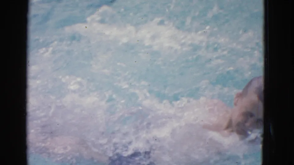 At the end of the clip, the swimmer's face is briefly visible near the edge of the pool frame as backstroke splashes fill the water.