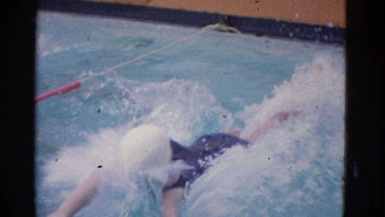 1953 Yonkers home-movie frame of a swimmer in a white cap practicing a stroke amid splashing pool water.