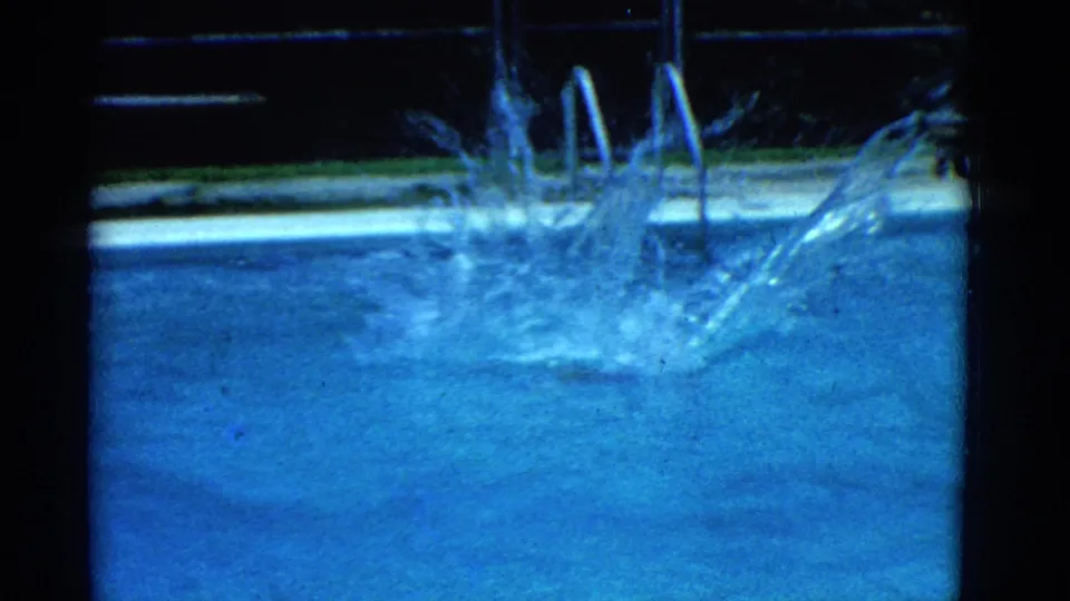 1953 Yonkers pool frame with a large splash where the swimmer has entered the blue water beside ladder rails.