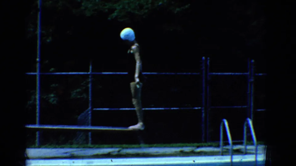 1953 Yonkers 8mm frame showing a swimmer standing on a narrow bench or board at a backyard pool with fencing behind.