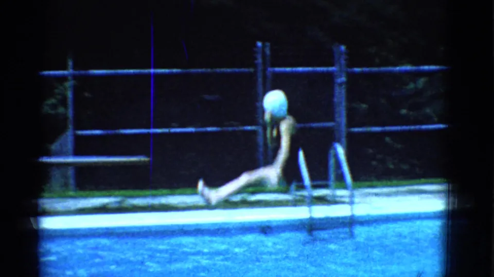 1953 Yonkers frame showing the swimmer seated at the pool edge near ladder rails, with blue water and fencing visible.