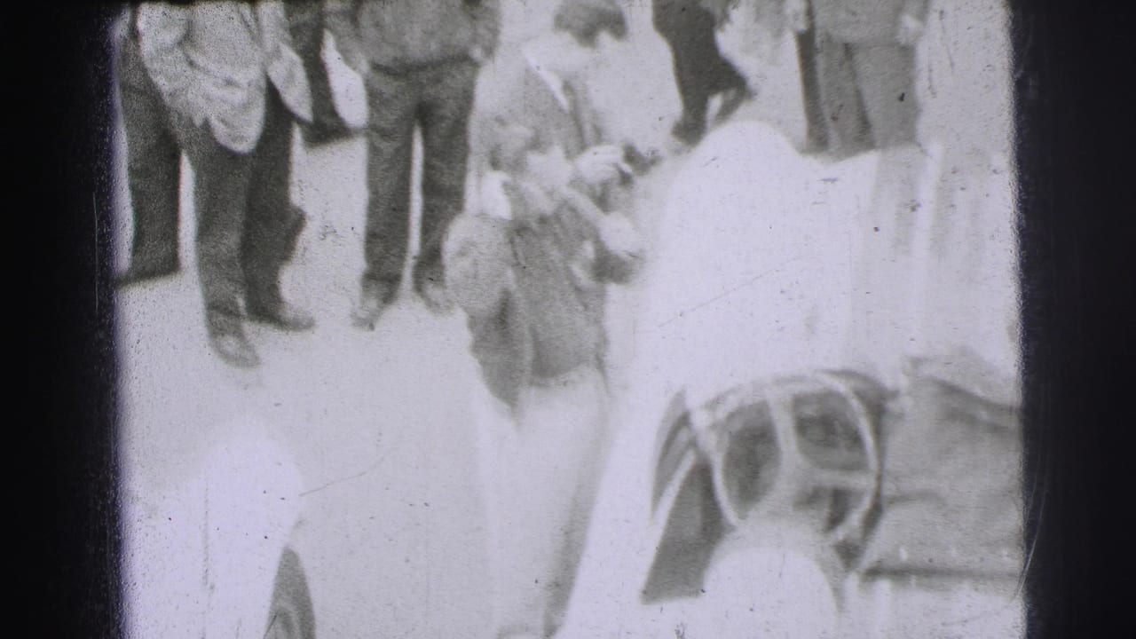 A 1954 Le Mans track-side view shows a man near an open racing car with other adult men standing in the background.