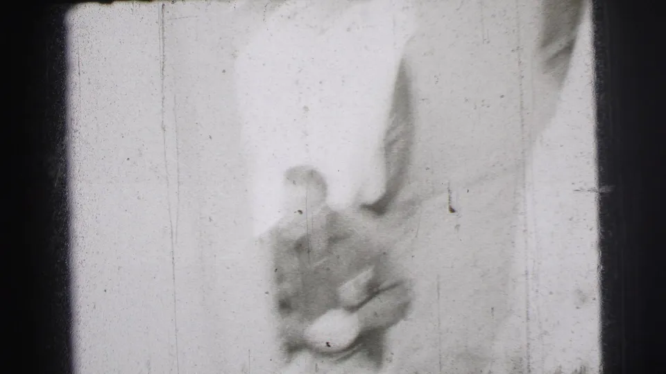 A soft, overexposed 1954 Le Mans frame shows a blurred adult man near a pale vertical surface with heavy film wear.
