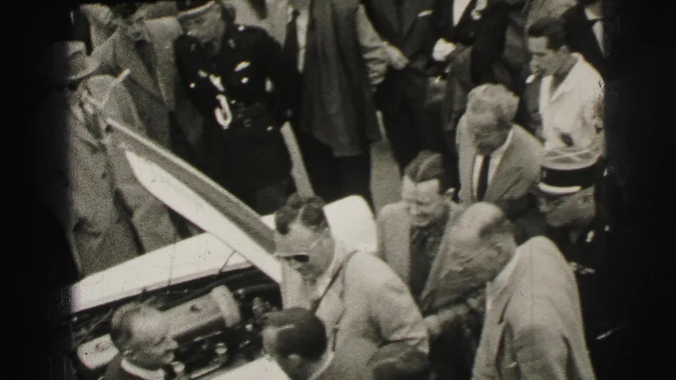 A 1954 Le Mans pit-side view shows several men clustered around the open hood of a race car during mechanical inspection.