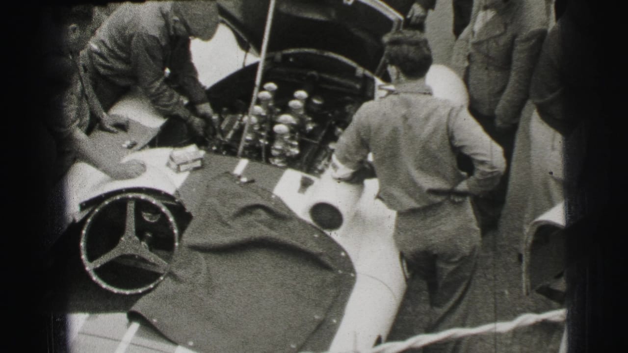 A mechanic reaches into the open hood area while a man stands beside the race car.