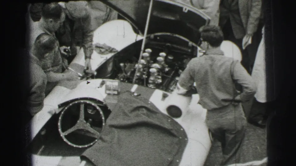 Mechanics and spectators look into the open hood of a Mercedes-Benz race car in 1954 Le Mans home-movie footage.