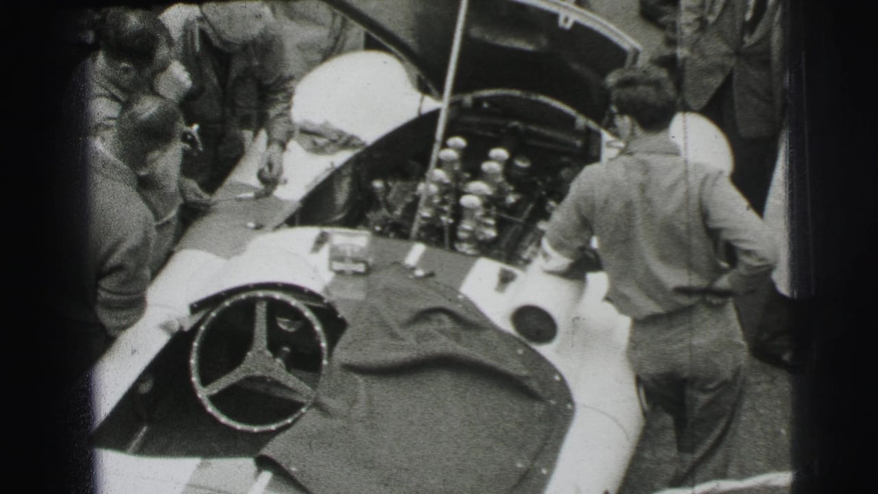 Mechanics lean over an open Mercedes-Benz race car in a crowded pit lane.