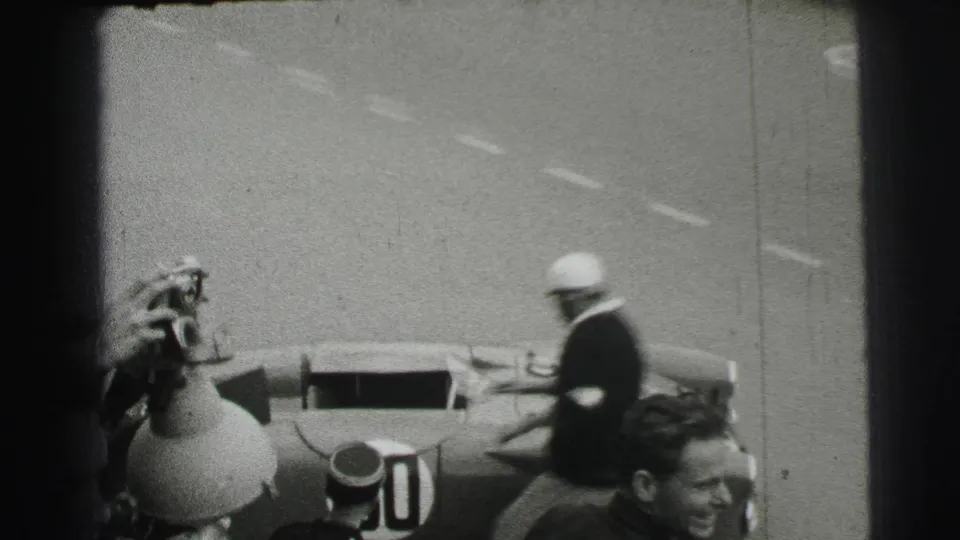 At Le Mans in 1954, a helmeted driver reaches an open-cockpit number 50 racing car while other people stand nearby.