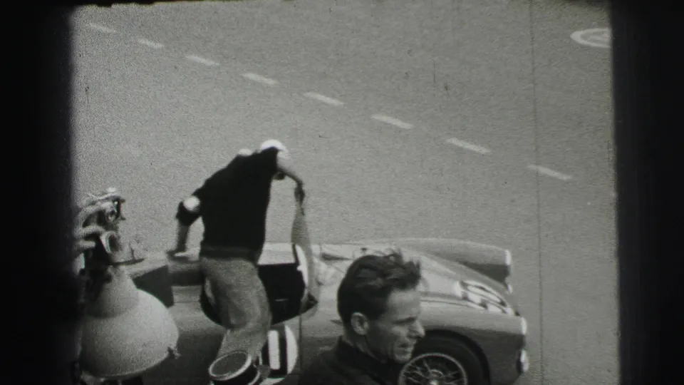 At Le Mans in 1954, the driver appears to climb into or lean over the number 50 car while a nearby man is visible in the foreground.