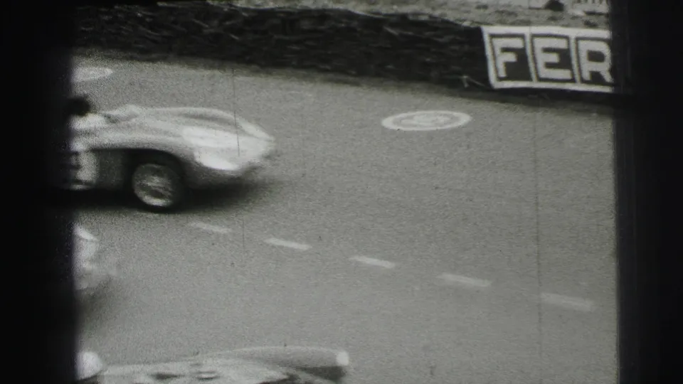 At Le Mans in 1954, a sports car blurs past on the track as a partial Ferodo sign and lane markings remain visible.