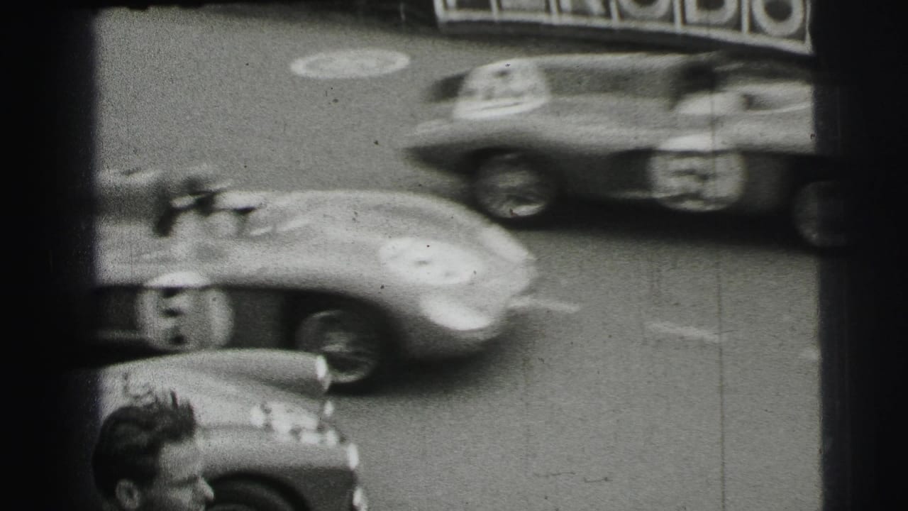 Black-and-white 1954 Le Mans home-movie frame showing blurred racing cars near Veedol trackside advertising and a spectator edge.