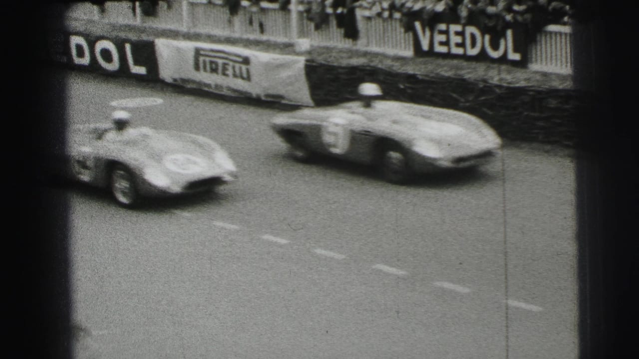 Two blurred race cars pass barriers with Pirelli and Veedol signage behind them.