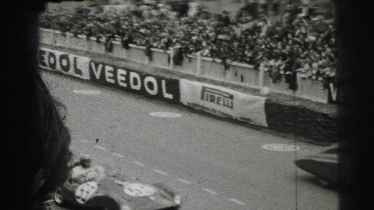 A spectator viewpoint over the Le Mans course shows crowded barriers, Veedol and Pirelli signage, and a race car partly visible at the bottom.