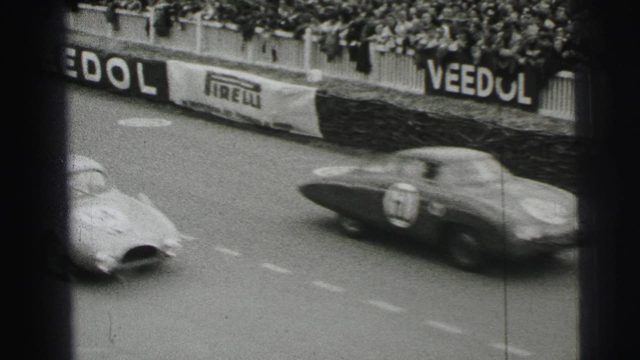 Race cars pass a track barrier in front of crowded grandstands with Veedol and Pirelli signs.