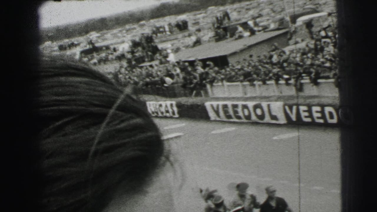 Spectator-shot 1954 Le Mans footage with a foreground head or hat obscuring part of the stands and branded barriers.