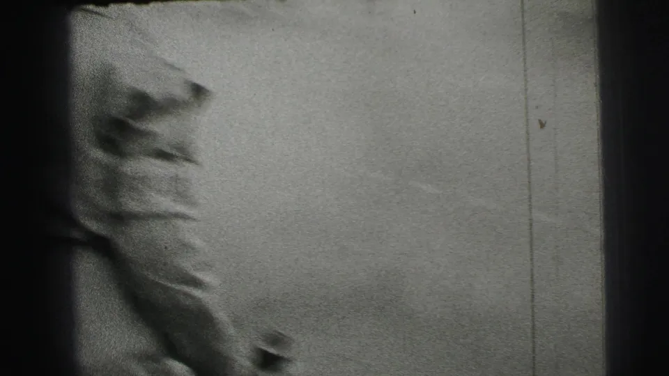 A cropped spectator or passerby appears close to the camera, with the racetrack surface and film scratches visible in the 8mm frame.