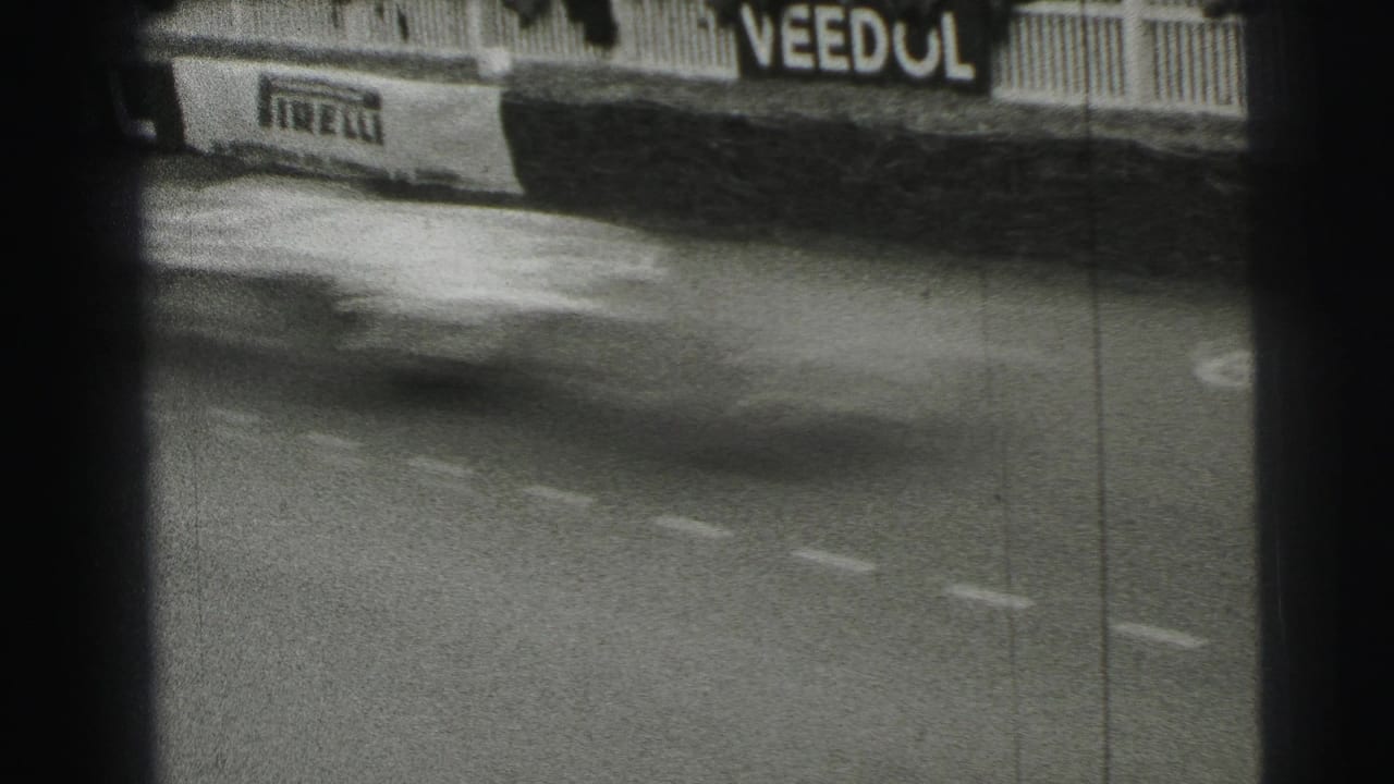 A fast-moving race car blurs across the Le Mans track, with Pirelli and Veedol sponsor boards behind it.