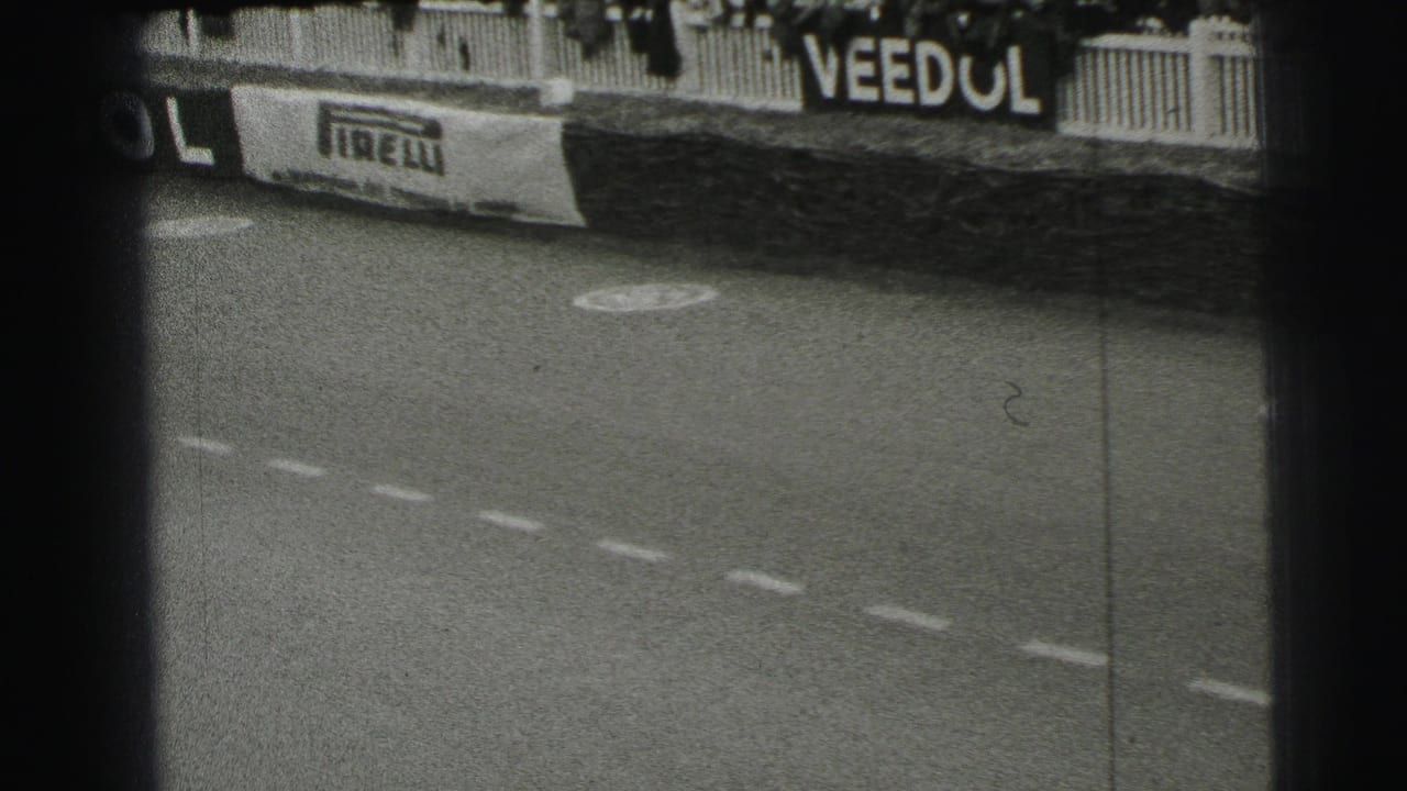 Le Mans trackside view after a car has passed, showing sponsor boards, barrier fencing, road markings, and grainy 8mm texture.