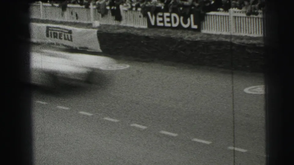1954 Le Mans 8mm frame with a blurred race car crossing the left side of the track near Pirelli and Veedol advertising.