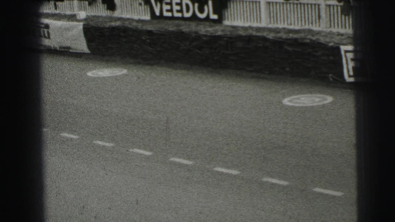 1954 Le Mans 8mm frame showing the track after a pass, with dashed markings, circular painted symbols, fence rails, and a Veedol sign.