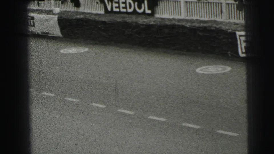 1954 Le Mans 8mm frame showing the track after a pass, with dashed markings, circular painted symbols, fence rails, and a Veedol sign.