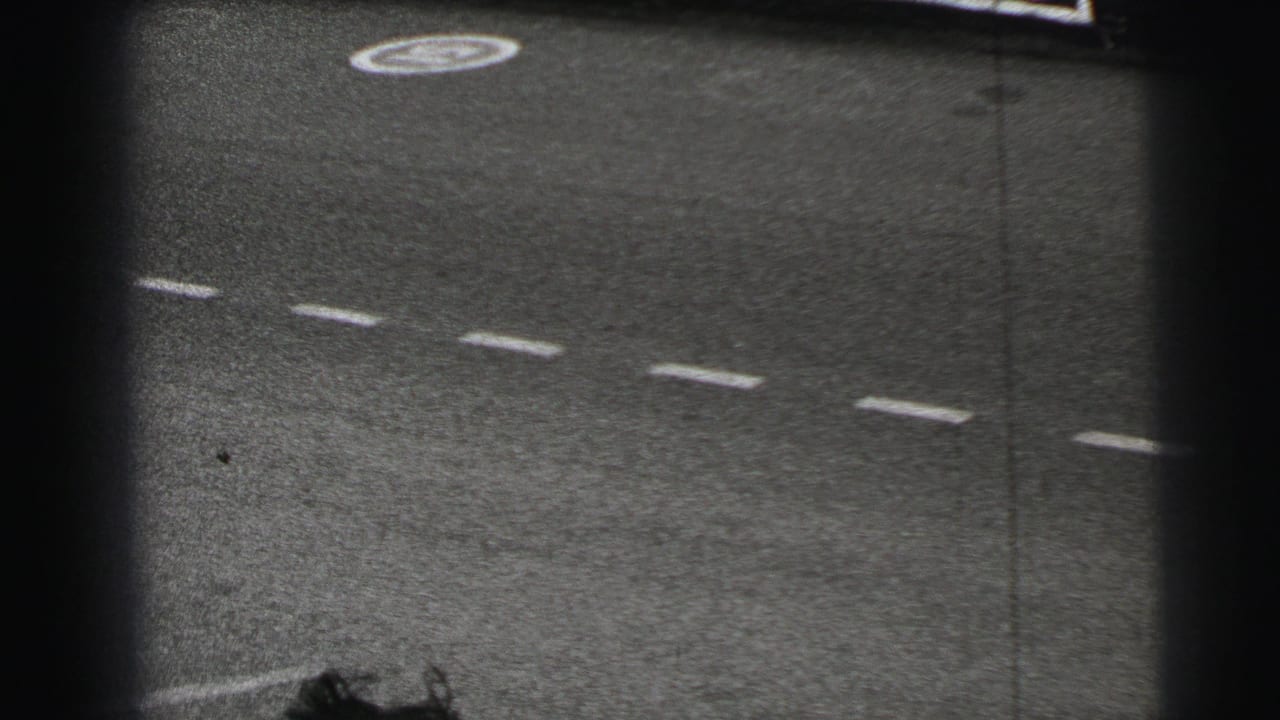 Final 1954 Le Mans frame after the pass, showing an empty paved track with dashed markings and a circular painted symbol.