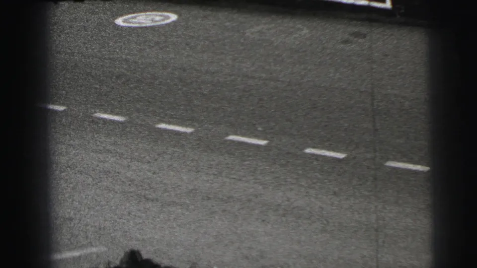 Black-and-white 8mm frame of the Le Mans track surface with painted lane markings and heavy film-edge shadow.