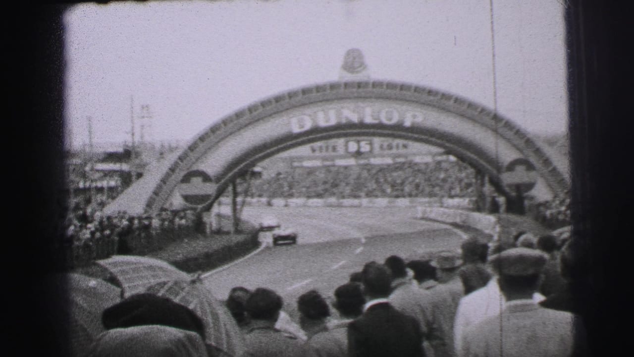 Le Mans race car passes under the Dunlop arch before a dense crowd of spectators in 1950s France.