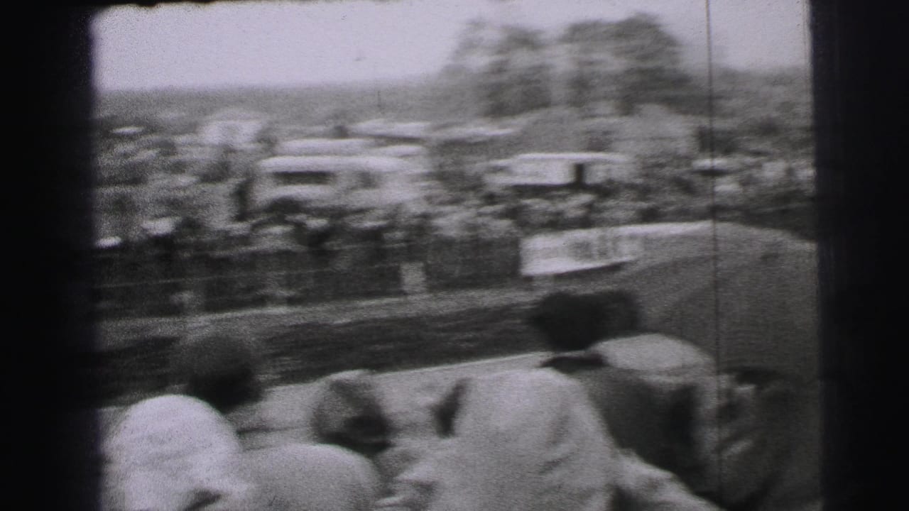 Motion-blurred 8mm view of a classic race car speeding past spectators at Le Mans in 1954 metadata context.