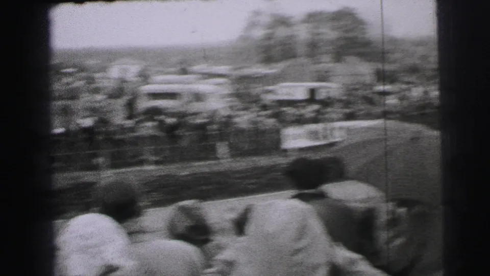 Motion-blurred 8mm view of a classic race car speeding past spectators at Le Mans in 1954 metadata context.