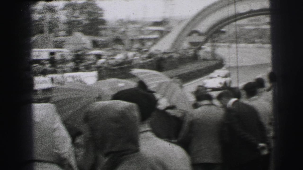 1954 Le Mans 8mm frame showing a wet trackside crowd watching race cars pass near the Dunlop bridge.