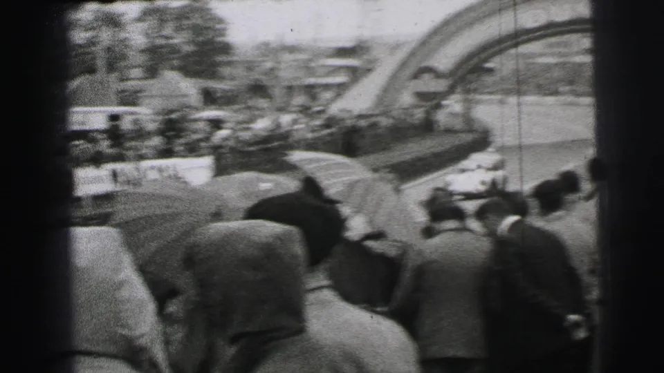 1954 Le Mans 8mm frame showing a wet trackside crowd watching race cars pass near the Dunlop bridge.