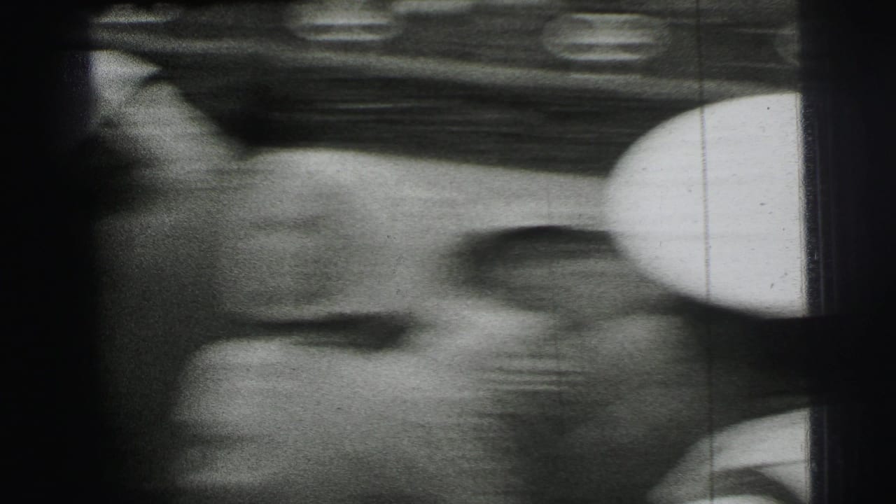 Soft, handheld 1954 Le Mans frame with a spectator in close view near umbrellas and the underside of a trackside structure.