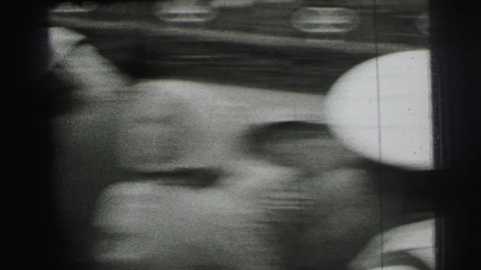 Soft, handheld 1954 Le Mans frame with a spectator in close view near umbrellas and the underside of a trackside structure.