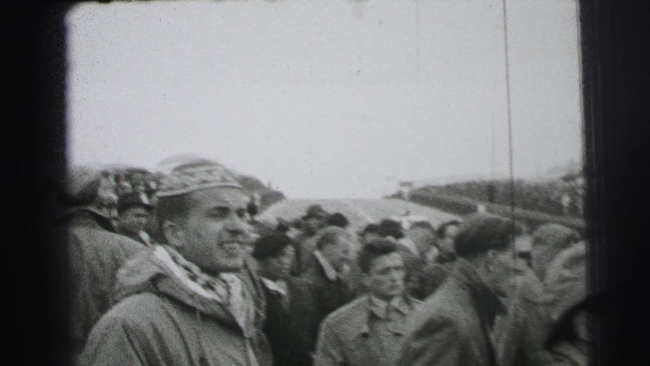 1954 Le Mans crowd view with a smiling man in a decorated hat and scarf standing among other spectators near the circuit.